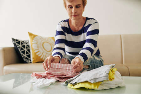 Smiling senior woman folding her clothes after washing and drying themの写真素材