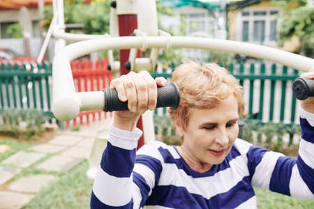Positive senior woman doing exercises on sport facility in city park