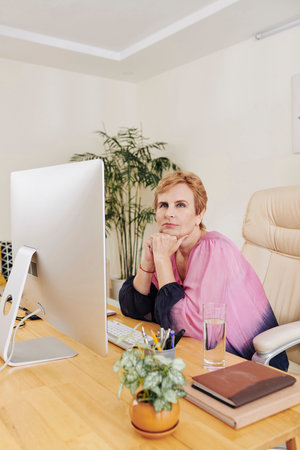 Portrait of pretty aged businesswoman contemplating about future when sitting at her office table