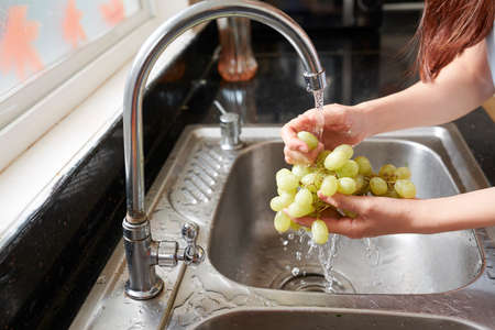 Close-up image of woman rinsing organic gren grape under cold tap water in kitchen sinkの写真素材