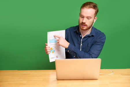 Young entrepreneur video calling coworker and explaining detail of financial report in his handsの写真素材