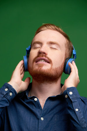 Handsome young bearded man closing eyes when listening to his favorite song in headphones