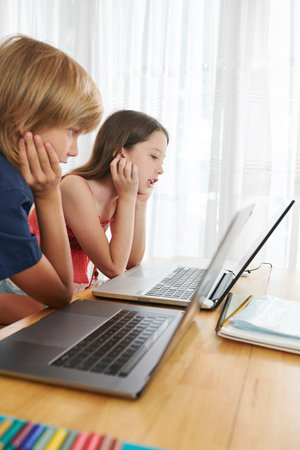 Children reading aloud articles on screens of laptops when they are studying online