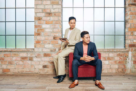 Happy young Vietnamese startuppers working in their loft office with brick walls and big windowsの写真素材