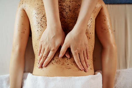 Hands of beautician scrubbing back of young female client, view from aboveの写真素材