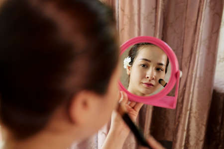 Beautiful young Vietnamese woman holding small round woman and applying foundation on her skinの写真素材