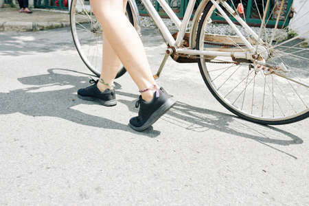 Legs of young woman with feet bracelets walking in street with her bicycleの写真素材