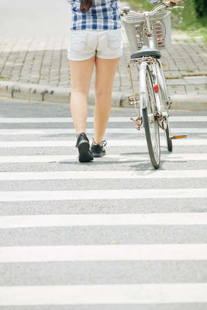 Rear view of young woman with bicycle crossing road in the cityの写真素材