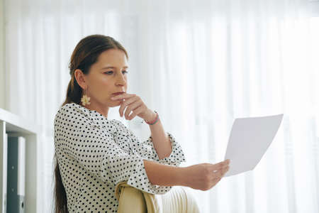 Portrait of pensive female entrepreneur reading document with good offer from investorの写真素材