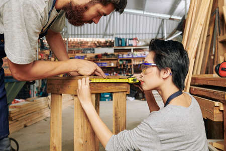 Professional carpenters using tape measure when checking size of stoolの写真素材