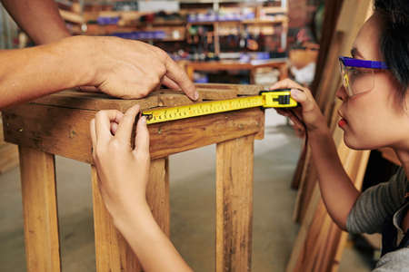 Close-up image of female carpenter measuring stool under control of coworkerの写真素材