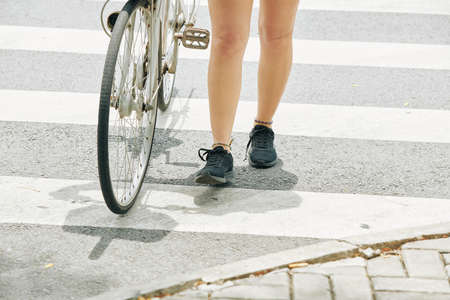 Fit legs of young woman standing on crossing road with her bicycleの写真素材