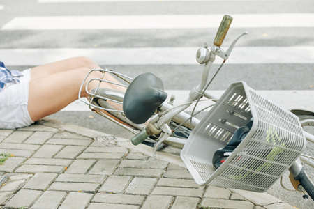 Young woman with injury lying on pavement after falling off bicycleの写真素材