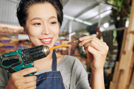 Smiling young Asian female carpenter putting screw on elongated drill bitの写真素材