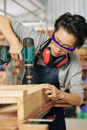 Young Asian carpenter worker wearing protective goggles when working with cordless screwdriverの写真素材