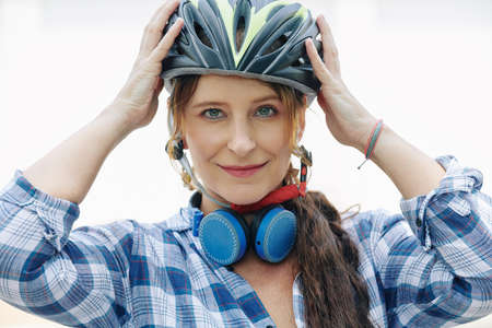 Portrait of smiling pretty woman with headphones around her neck putting on helmetの写真素材