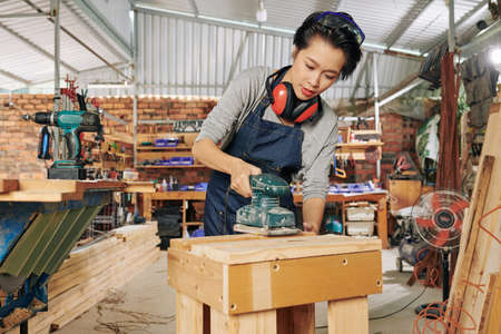 Professional female carpenter polishing wooden surface of table she made in workshopの写真素材