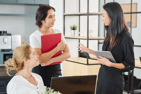 Three young multi-ethnic businesswomen standing and talking to each other during working day at officeの写真素材