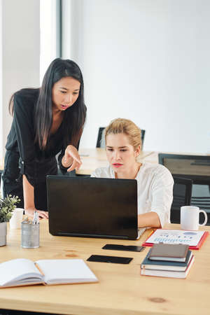 Two young businesswomen using laptop computer in work while working at the workplace at officeの写真素材