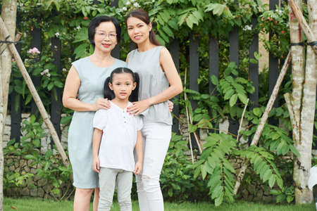 Portrait of Asian family generation standing outdoors and smiling with green trees in the backgroundの写真素材