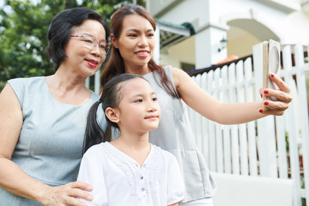 Asian family of three mother daughter and grandmother posing on mobile phone for selfie portrait...