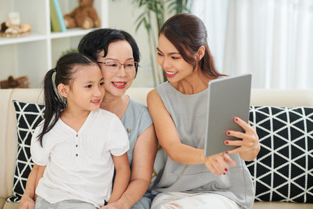 Asian happy family mother daughter and grandmother sitting on sofa together and communicating with...