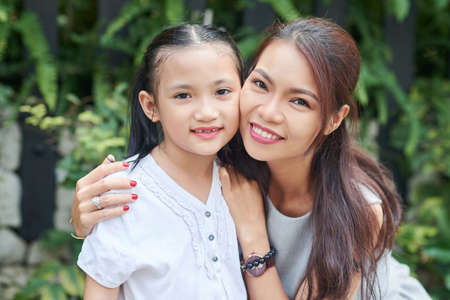 Portrait of Asian family of two mother and daughter embracing and smiling at camera outdoorsの写真素材
