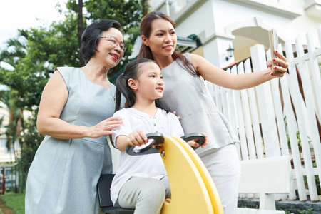 Asian family generation making selfie portrait on mobile phone while playing together on their back yardの写真素材