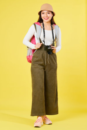 Cheerful young Vietnamese woman with backpack and digital camera smilng at camera, isolated on...