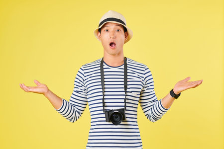 Shocked tourist with digital camera making helpless gesture, opening mouth and looking at camera