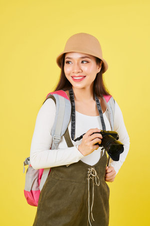 Portrait of smiling pretty woman in panama hat holding digital camera and looking away, isolated on...