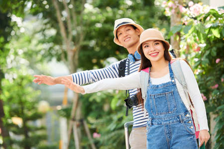 Smiling young Asian couple in hats sticking out arms to catch taxi in the streetの写真素材