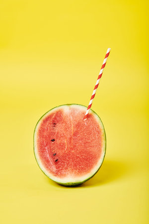 Half of watermelon with striped red and white plastic drinking straw, isolated on yellow