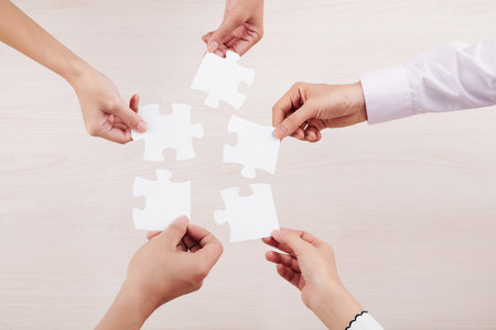 Close-up of team connecting their puzzles and demonstrating unity of friendship isolated on white...