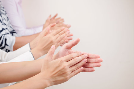 Close-up of group of business people clapping hands together while standing against the white...