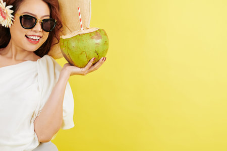 Portrait of beautiful young tourist wearing sunglasses drinking coconut and looks very happy over...