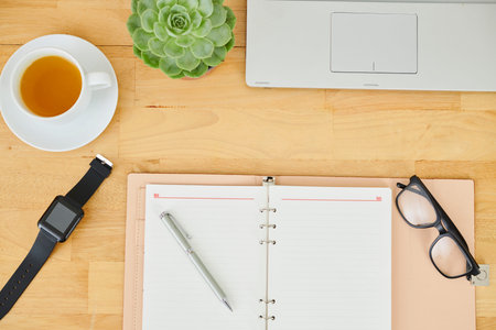 Close-up of opened notepad with blank sheets eyeglasses watches and cup of tea on wooden office desk