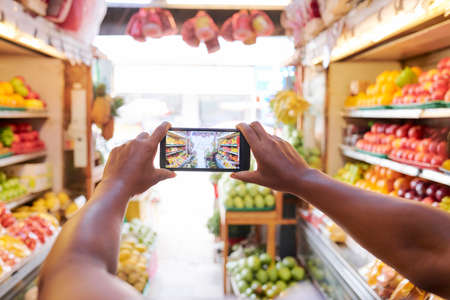 Close-up of female hands holding mobile phone and taking a photo of supermarket with fruits and vegetables departmentの写真素材