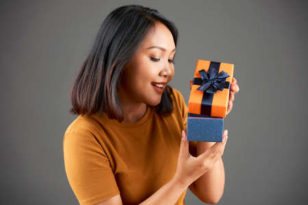 Asian young woman with short black hair opening gift box and smiling isolated on grey backgroundの写真素材