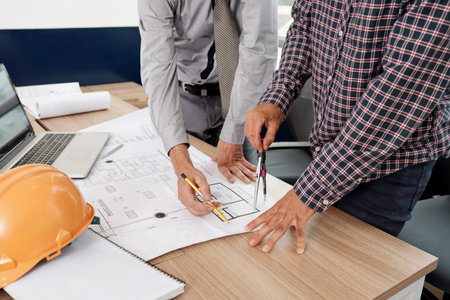 Close-up of two engineers standing near the table and drawing construction blueprint of new building...