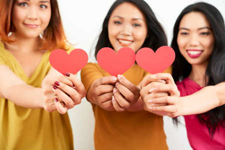 Portrait of group of Asian friends holding postcards in the shape of red hearts smiling and showing them to the cameraの写真素材