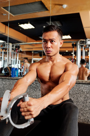 Strong fit Vietnamese man training on row machine in gym