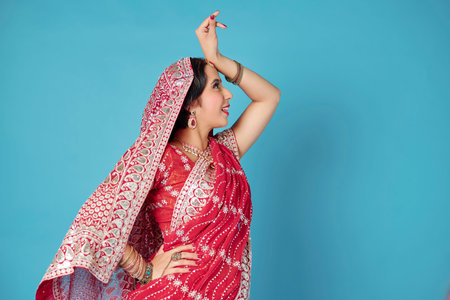 Happy young Indian woman in national costume dancing against blue background