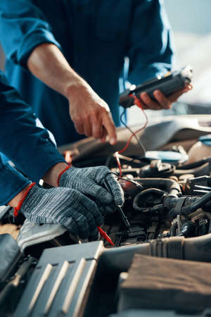 Mechanics using professional multimeter to check voltage level of car batteryの写真素材