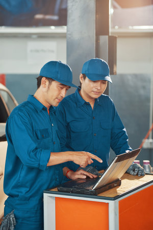 Vietnamese car service workers discussig information on laptop screen when working in garage