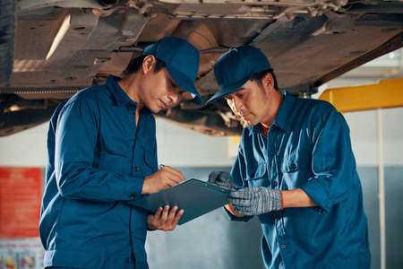 Professional experienced Vietnamese mechanics checking list of car problems after inspecting itの写真素材