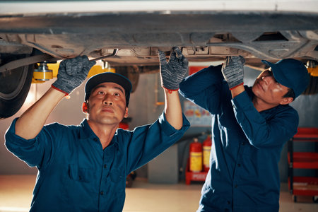 Professional mechanics with dirt on faces attaching front car suspention after diagnostics