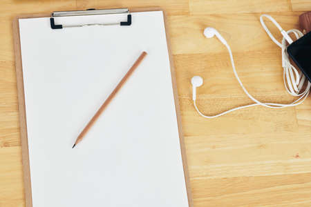 Clipboard with blank paper sheet, pencil and earphones on wooden tableの写真素材
