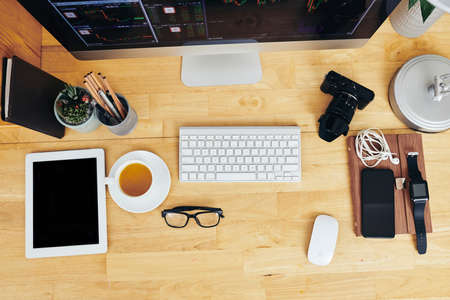 Gadgets, cup of tea and glasses on wooden desk of office worker, view from aboveの写真素材