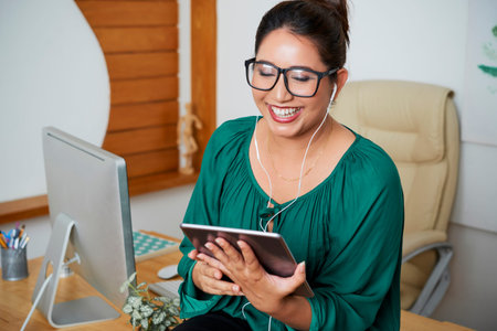 Successful businesswoman in eyeglasses wearing headphones and has online conversation on digital...